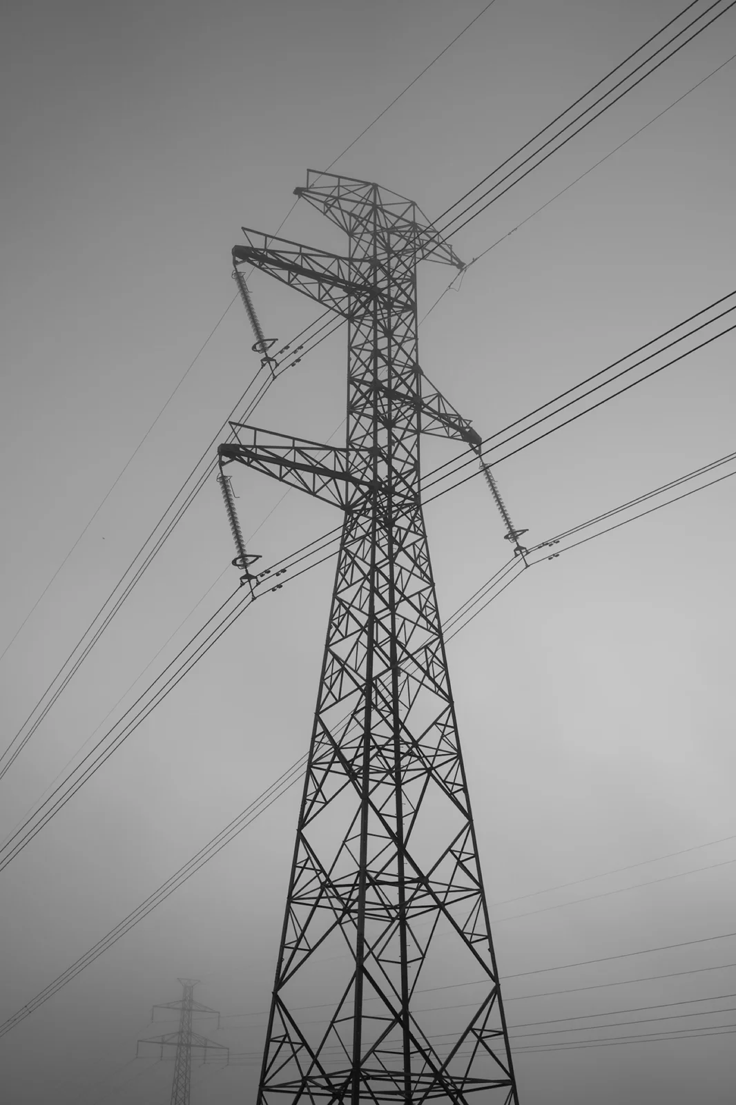 A black-and-white view looking up at an electricity pylon and overhead wires.